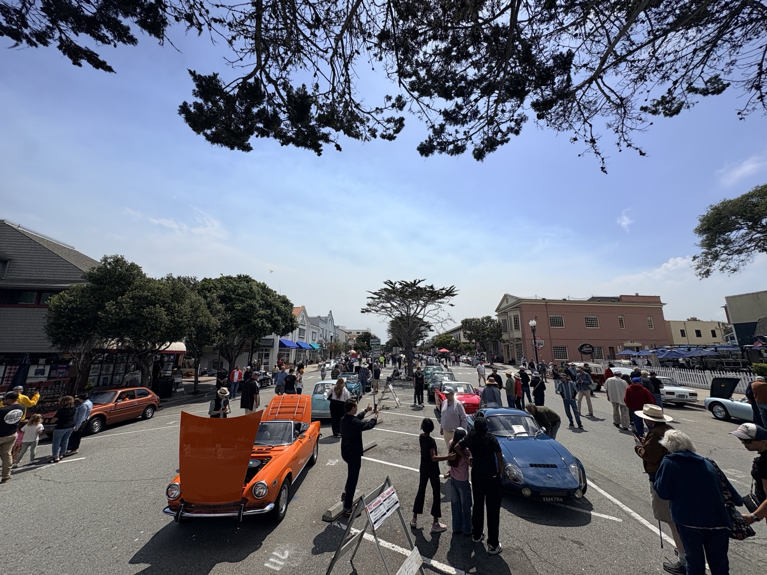 Rows of compact vintage cars and spectators filling sunny Lighthouse Avenue during Pacific Grove's 2026 Little Car Show
